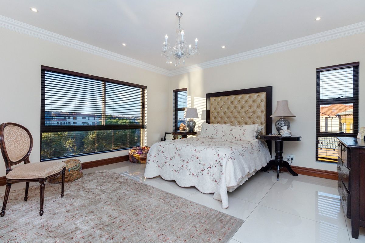 Spacious bedroom featuring polished tile flooring, crown molding, recessed lighting, a decorative chandelier, and large windows with fitted venetian blinds.