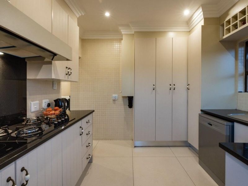 A well-maintained kitchen featuring light-toned cabinetry, dark stone countertops, a gas hob with extractor, and tiled splashbacks with ample storage space.