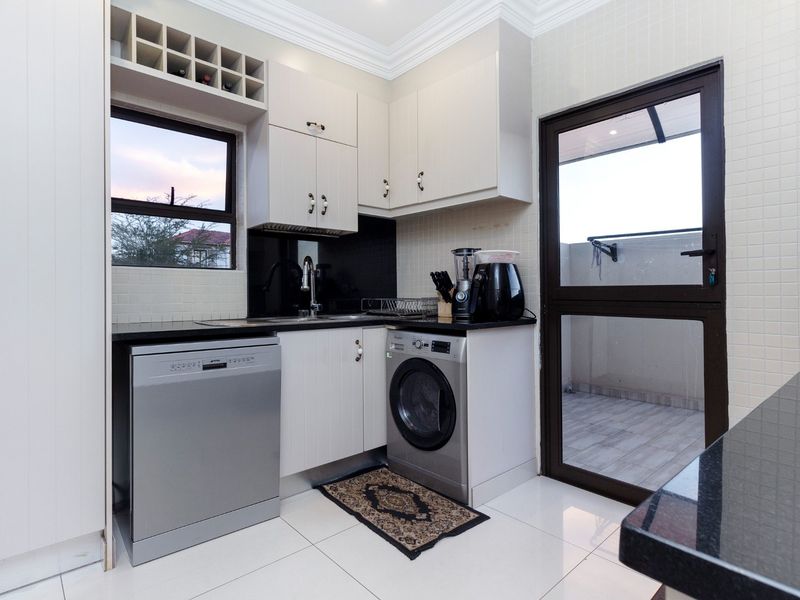 A well-maintained scullery featuring built-in cabinetry, granite countertops, a stainless steel sink, and direct access to an outdoor area.