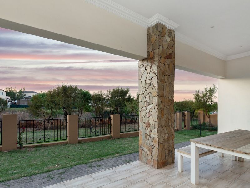 A covered patio featuring a stone-clad pillar, tiled flooring, and recessed lighting, overlooking a landscaped garden with wrought iron fencing.