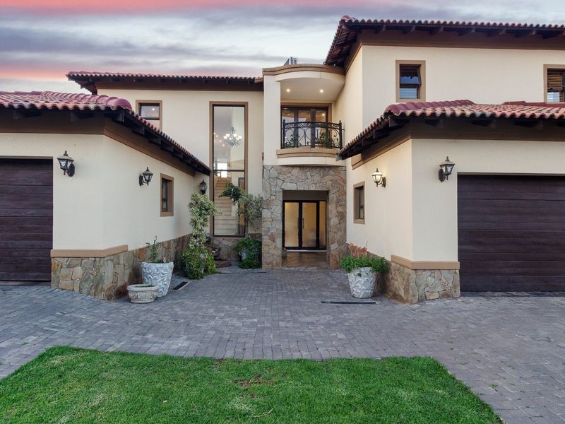 Impressive double-storey residence featuring a paved driveway, double garages, stone-clad accents, and a prominent entrance with a balcony.