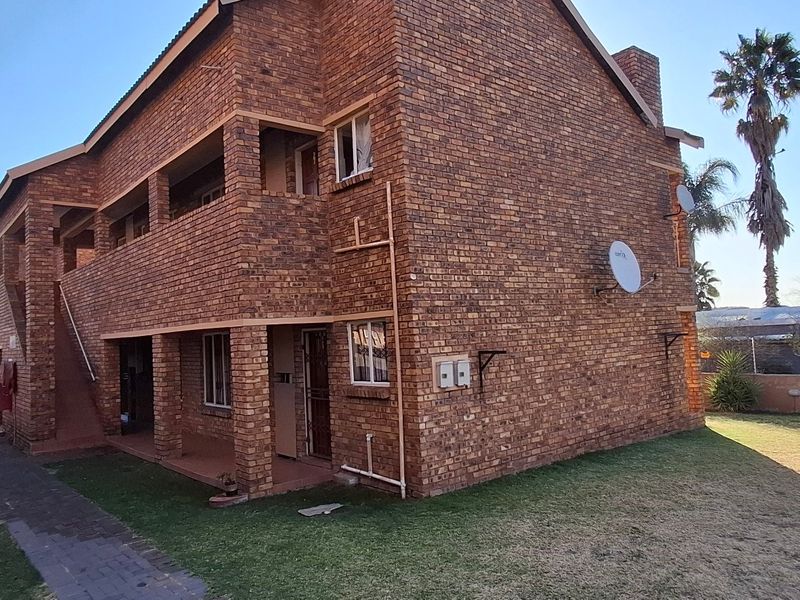 Rear view of a multi-story face brick townhouse complex featuring covered ground-floor patios, upper-level balconies, and surrounding lawn areas.