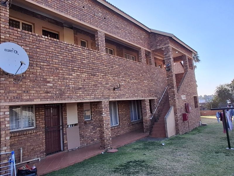 Rear view of a multi-story face brick townhouse complex featuring external staircases, security gates, and a shared garden area.