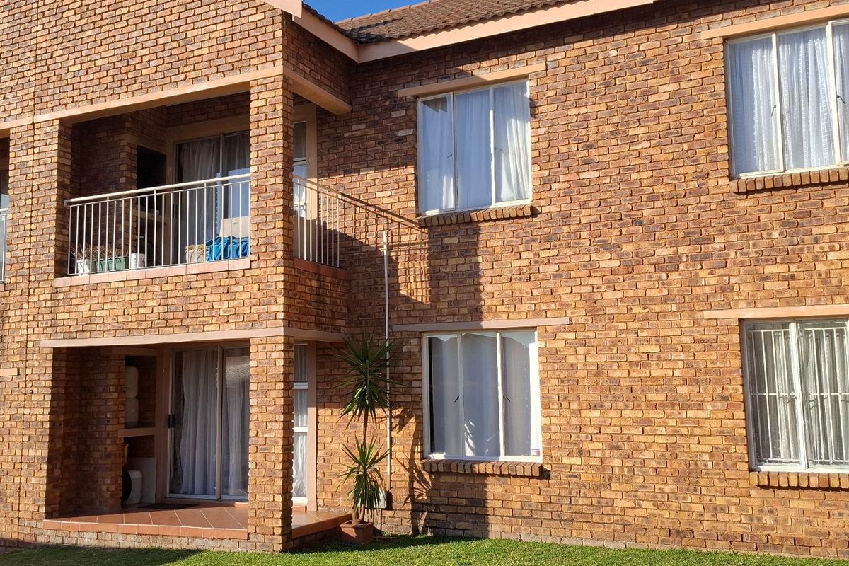 Rear view of a double-story townhouse featuring face brick construction, a private balcony with metal railings, and a ground-floor patio area.