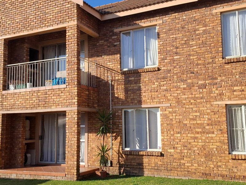 Rear view of a double-story townhouse featuring face brick construction, a private balcony with metal railings, and a ground-floor patio area.