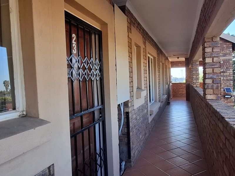 A covered exterior balcony featuring tiled flooring, brick wall finishes, and a secure entrance gate, providing access to the townhouse unit.