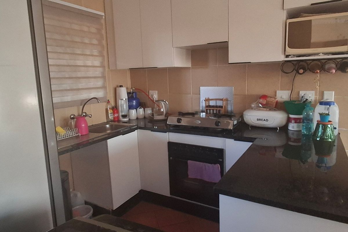 Compact kitchen featuring white cabinetry, granite countertops, a gas hob, built-in oven, and tiled backsplash with a functional layout.