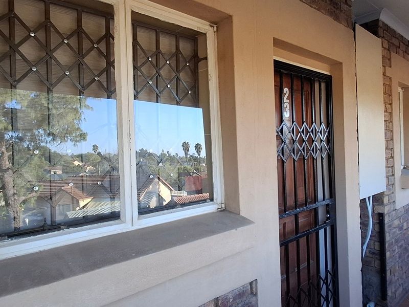 Front entrance view of a townhouse featuring a security gate, security bars on windows, and a tiled walkway along the brick facade.