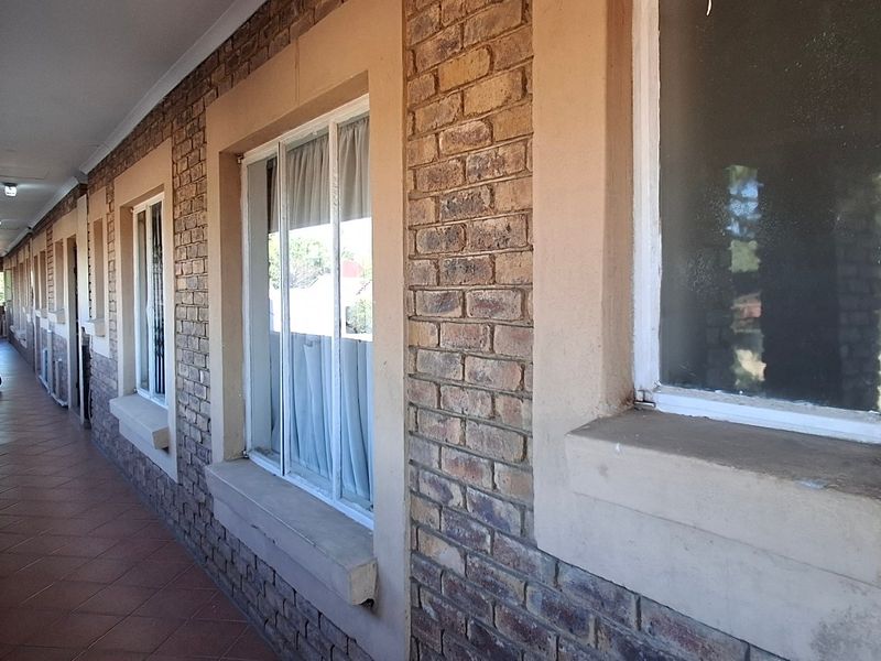An exterior covered walkway featuring exposed brick walls, tiled flooring, and multiple window access points along the townhouse building facade.