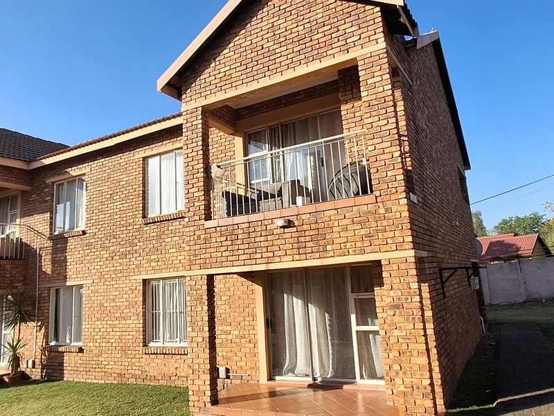 Rear view of a double-story face brick townhouse featuring upper-level balconies with metal railings and ground-floor patio access.