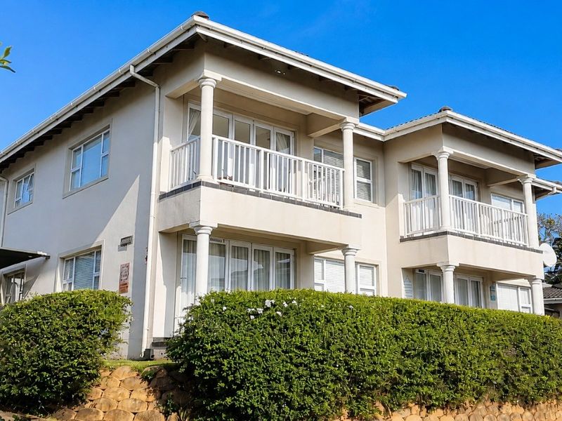 A well-maintained multi-story apartment building featuring private balconies with white railings, classic columns, and a tiled roof exterior.
