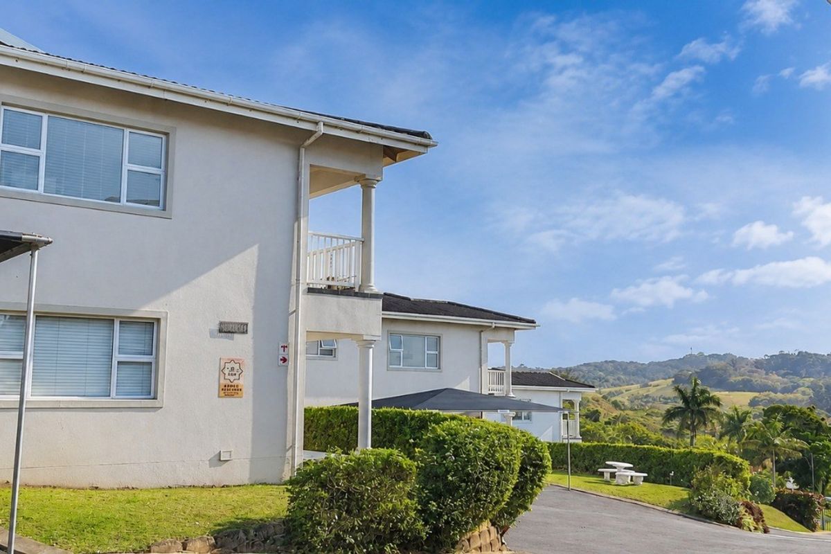 Exterior view of apartment complex buildings featuring balconies, paved driveways, carports, and landscaped garden areas with scenic hillside views.