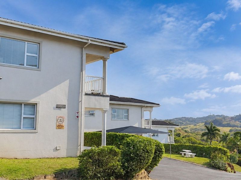 Exterior view of apartment complex buildings featuring balconies, paved driveways, carports, and landscaped garden areas with scenic hillside views.