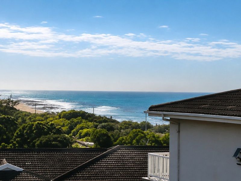 Elevated coastal view overlooking the ocean, beach, and surrounding coastal vegetation from an apartment balcony.
