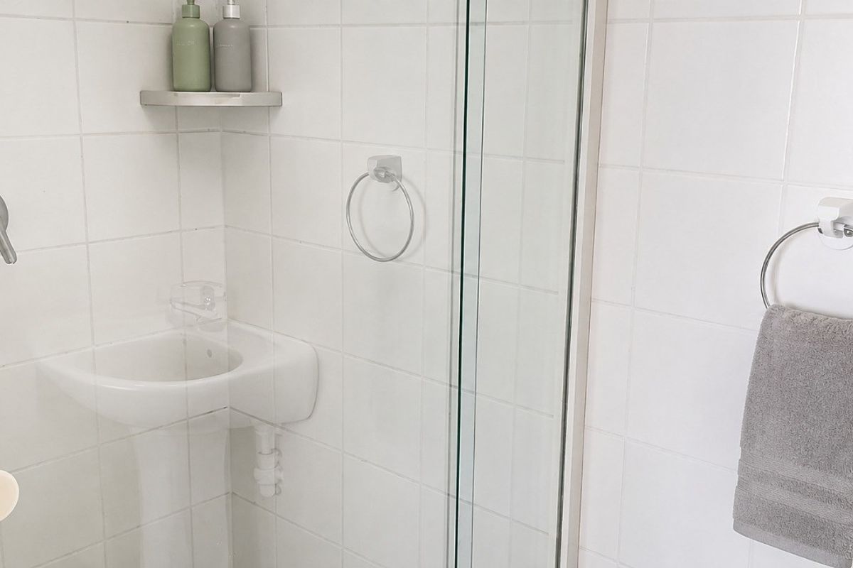 A compact bathroom featuring white wall tiles, a pedestal basin with a mixer tap, and a glass-enclosed shower area.