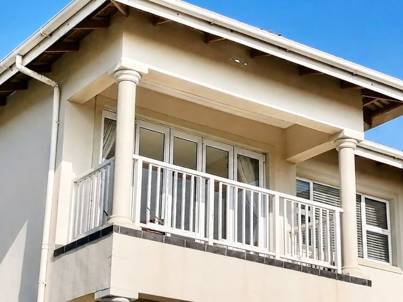 A well-maintained upper-level balcony featuring classic columns, white railings, and large sliding glass doors providing access to the interior.