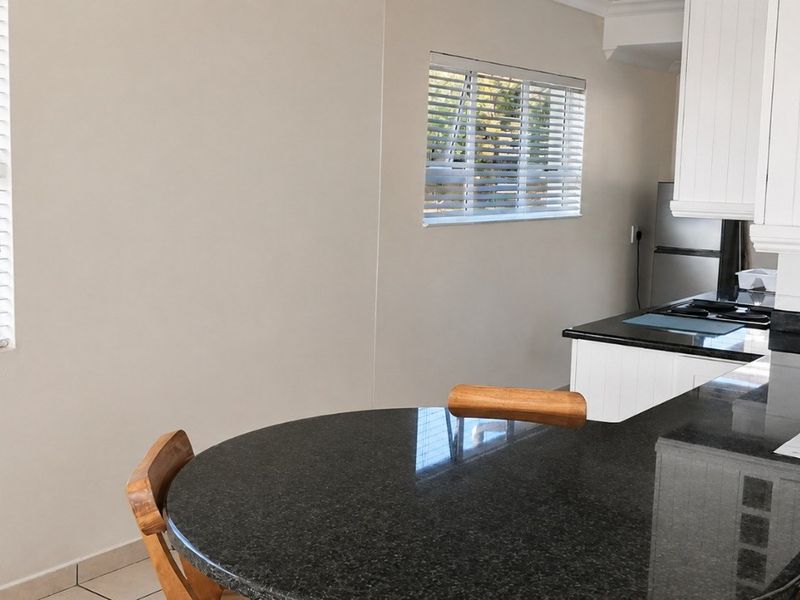 A functional kitchen featuring white cabinetry, dark granite countertops, and a built-in hob, with natural light provided by two windows with venetian blinds.