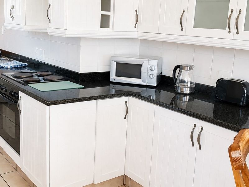 A functional kitchen featuring white cabinetry, dark granite countertops, a built-in oven, electric hob, and a double sink with tiled flooring.