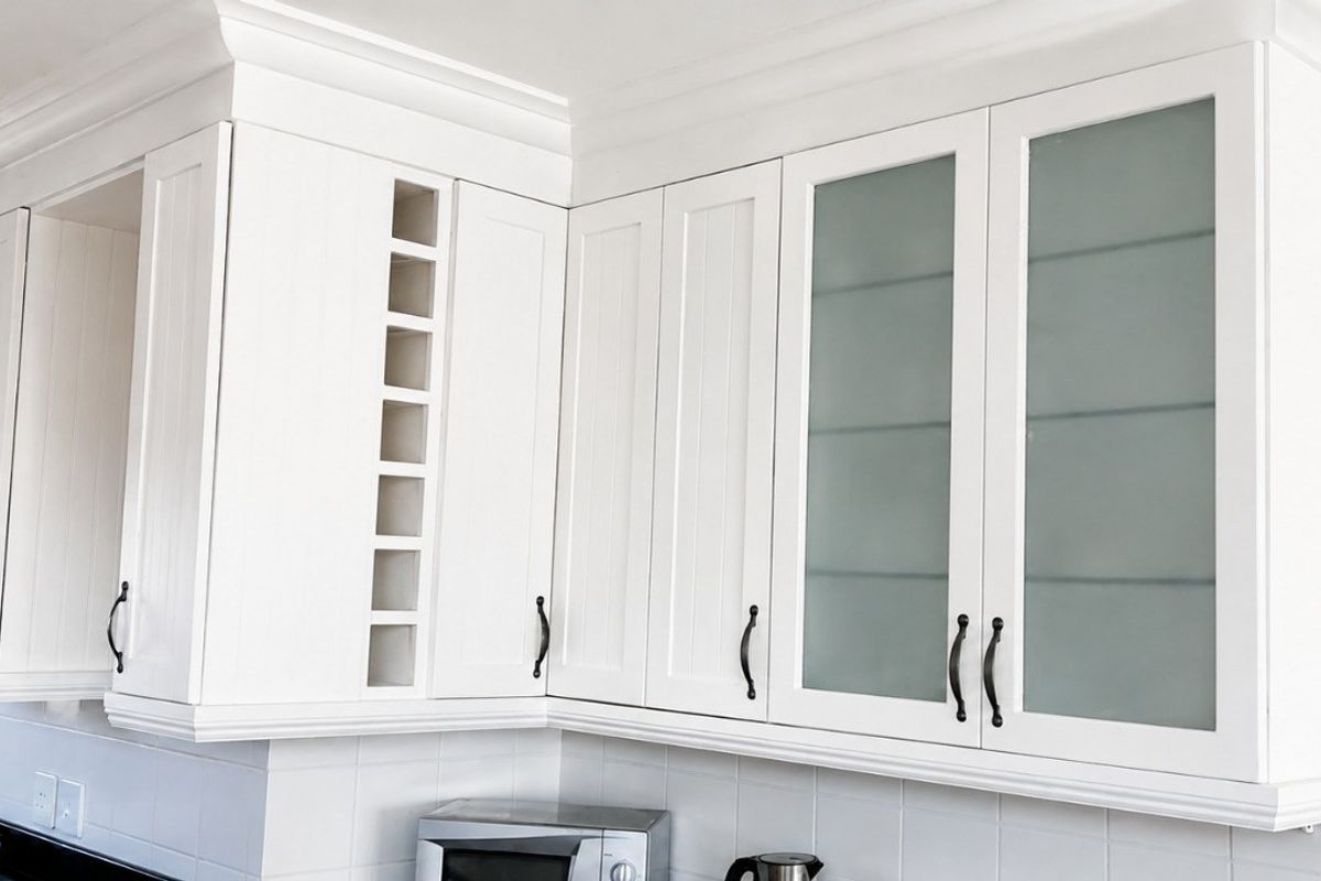 A well-maintained kitchen featuring white cabinetry with frosted glass inserts, crown molding, black granite countertops, and a tiled backsplash.