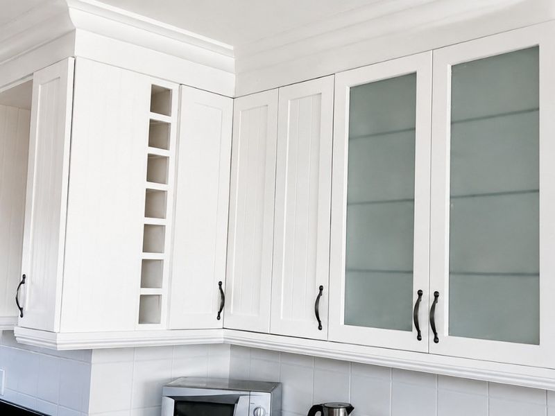 A well-maintained kitchen featuring white cabinetry with frosted glass inserts, crown molding, black granite countertops, and a tiled backsplash.