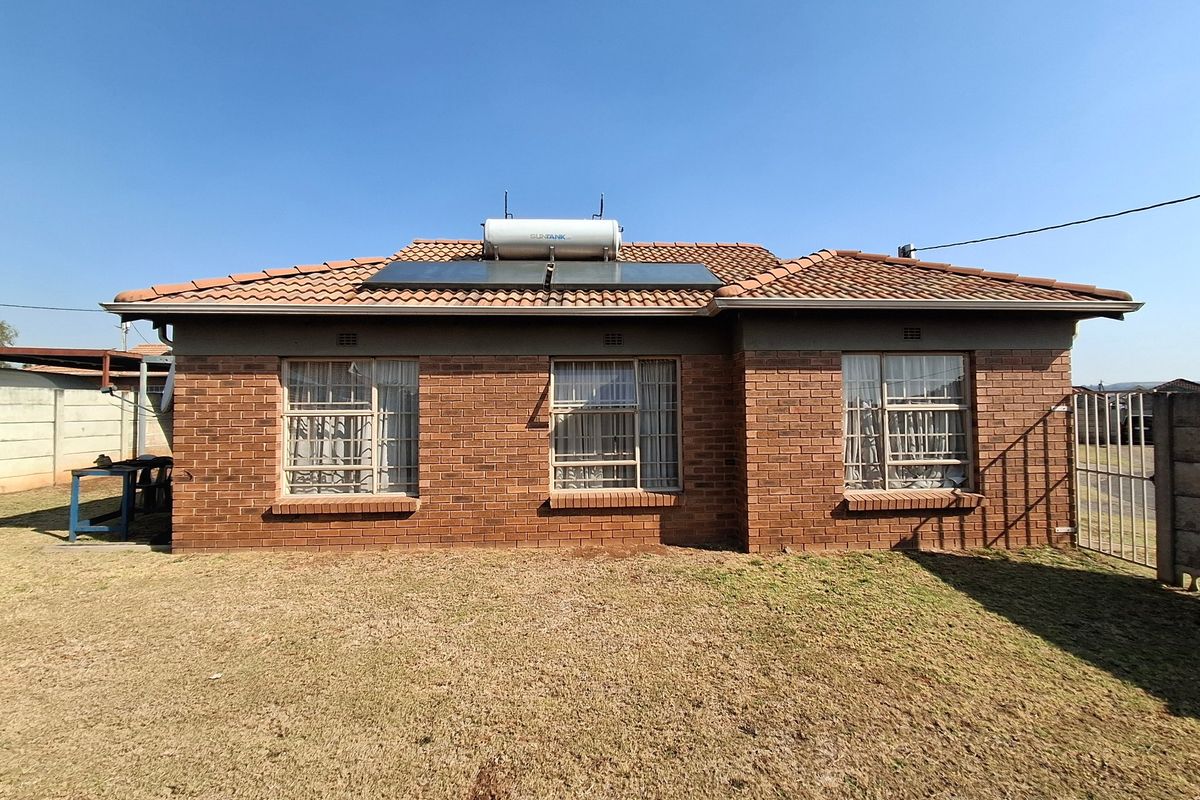 Rear view of a facebrick house featuring a tiled roof, solar water heating system, and secure aluminium-framed windows overlooking a lawn.