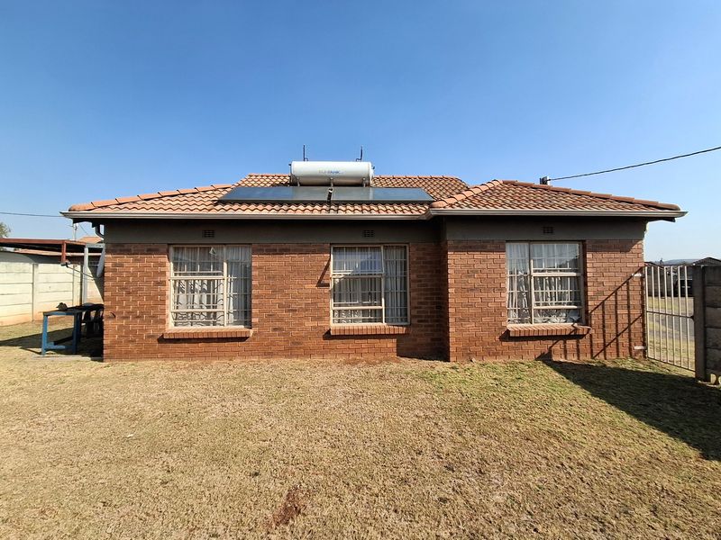 Rear view of a facebrick house featuring a tiled roof, solar water heating system, and secure aluminium-framed windows overlooking a lawn.