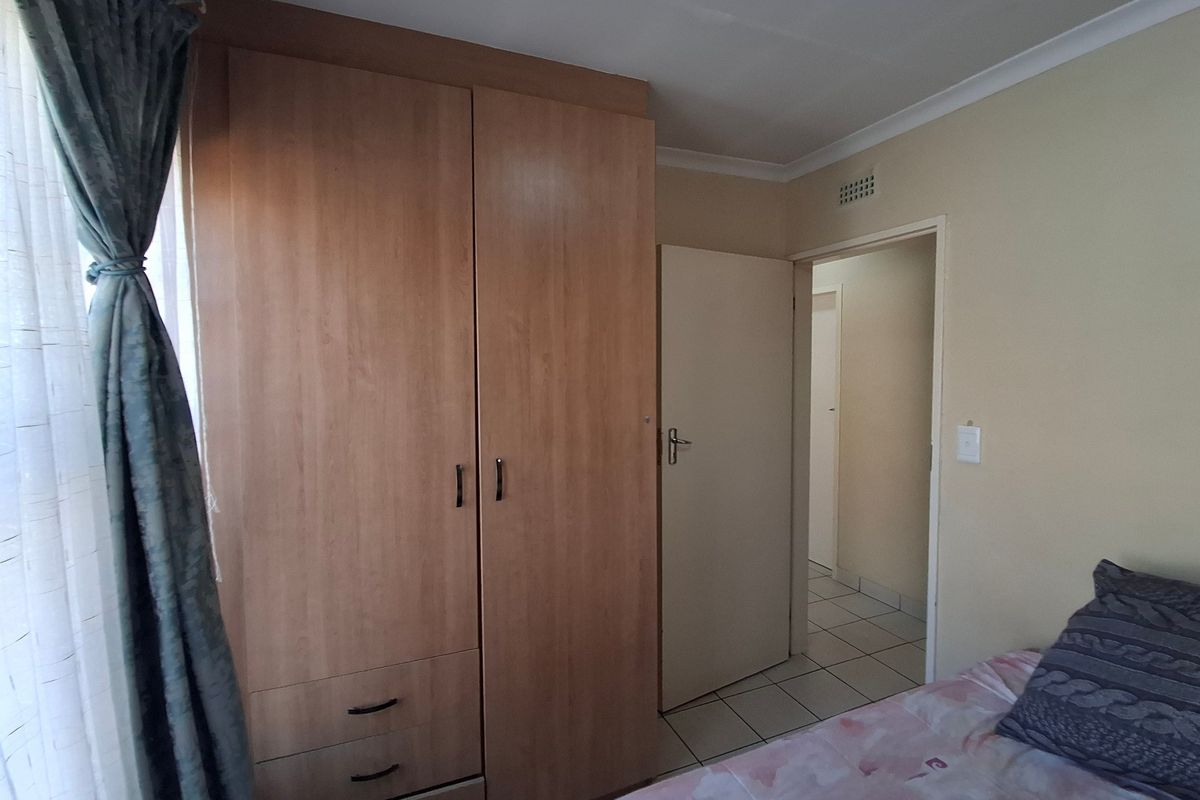 A bedroom featuring built-in wooden cupboards, tiled flooring, and neutral wall finishes, providing a functional and tidy living space.
