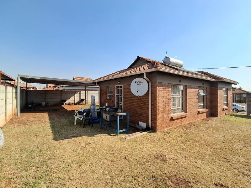 Rear view of a face brick house featuring a solar water heater, a detached carport, and a spacious backyard enclosed by precast concrete walls.
