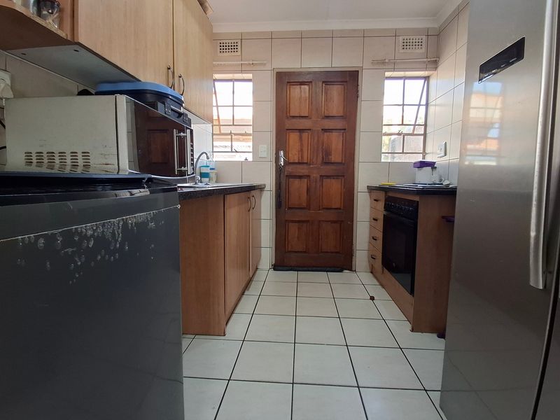 A functional kitchen featuring laminate cabinetry, built-in oven, hob, tiled splashbacks, and direct access to the exterior via a timber door.