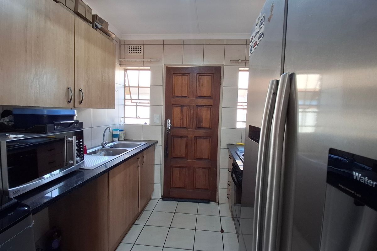 A functional kitchen featuring laminate cabinetry, granite countertops, a double stainless steel sink, and ceramic tiled flooring with direct access to an exterior door.