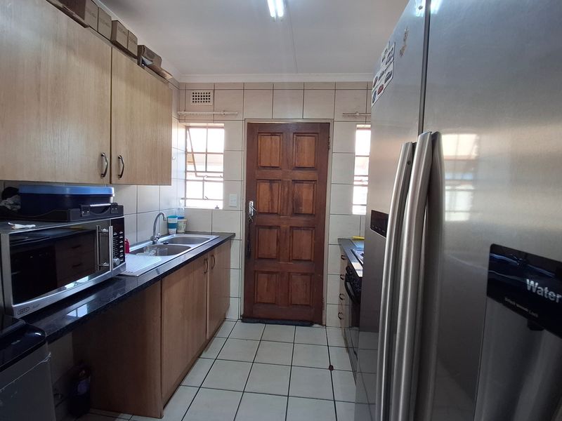 A functional kitchen featuring laminate cabinetry, granite countertops, a double stainless steel sink, and ceramic tiled flooring with direct access to an exterior door.
