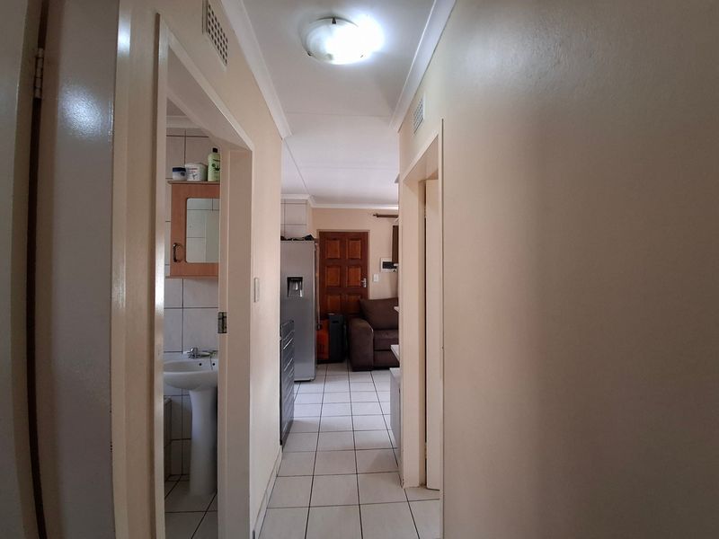 A view through a tiled hallway leading towards a living area, with a small bathroom visible to the left featuring a pedestal basin.