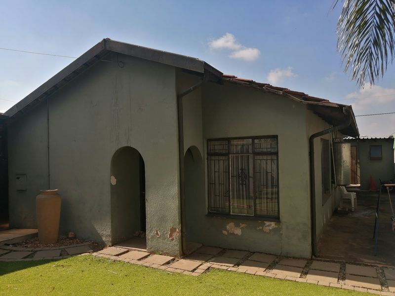 Front elevation of a single-story house featuring an arched entrance, tiled roof, and paved walkway, showing signs of exterior wear and paint deterioration.