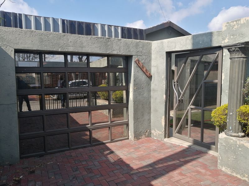 Front exterior view featuring a modern sectional garage door, glass entrance door, and brick paved driveway with a concrete boundary wall.