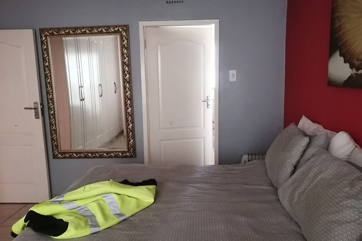 A bedroom featuring built-in cupboards, internal doors, and a ventilation grille, with a neutral and red accent wall finish.