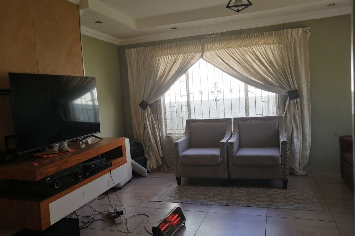 A living room featuring tiled flooring, recessed ceiling lighting, and a window fitted with security bars.