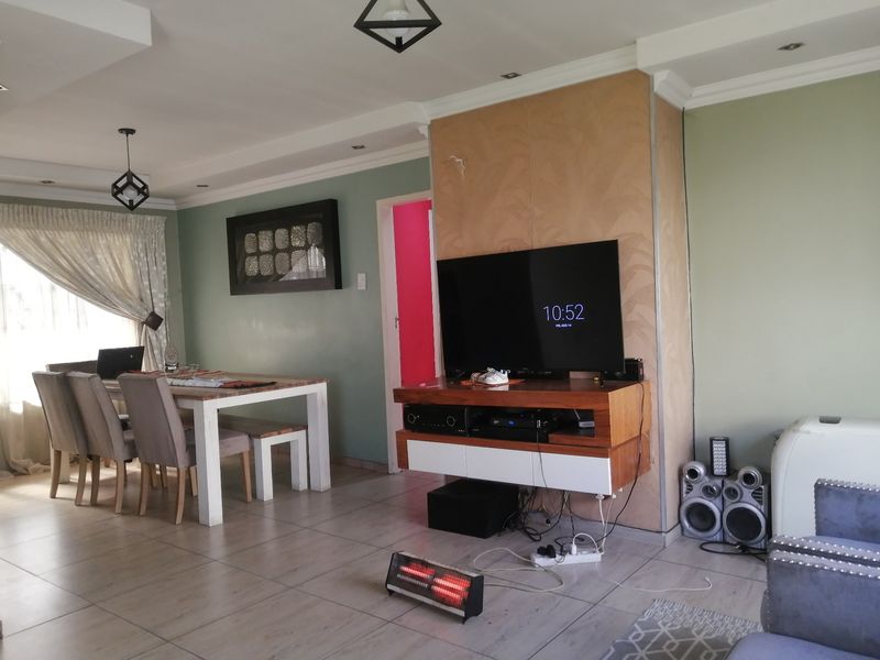 Open-plan living and dining area featuring tiled flooring, recessed ceiling lights, and a central feature wall panel.