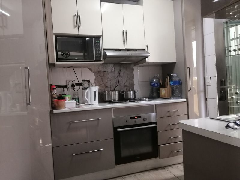 A compact kitchen featuring built-in cabinetry, an integrated oven, and extractor fan, currently showing visible damage to the wall tiling and exposed electrical wiring.