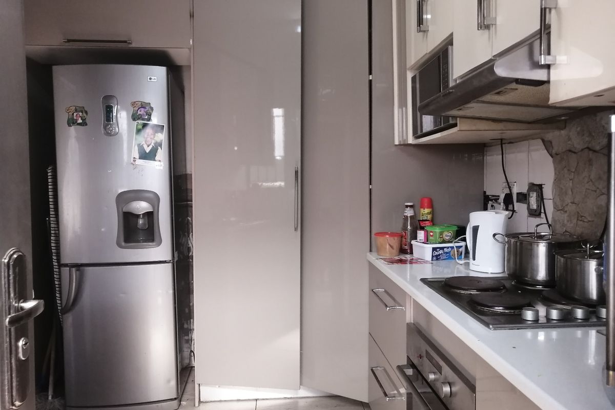 A compact kitchen featuring modern high-gloss cabinetry, a built-in oven and hob, extractor fan, and stone countertops.