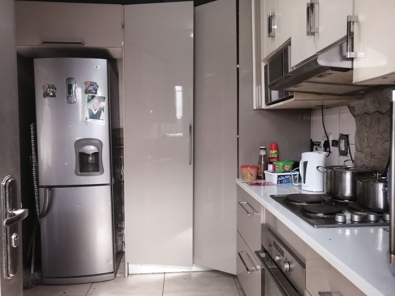 A compact kitchen featuring modern high-gloss cabinetry, a built-in oven and hob, extractor fan, and stone countertops.