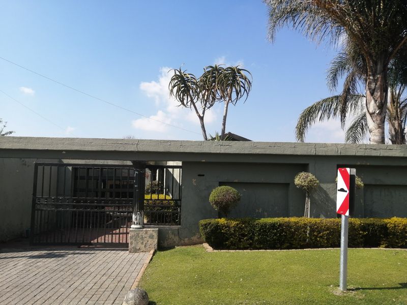 Front view of the property featuring a paved driveway, metal gate, and a boundary wall with established garden landscaping.
