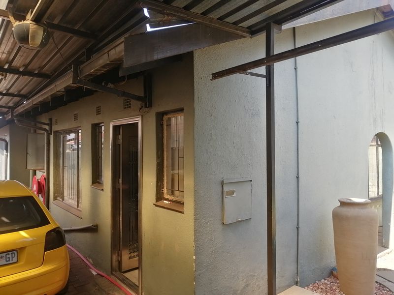 Rear exterior view of the property showing a covered walkway, security features, and visible wear to the roof and exterior wall finishes.
