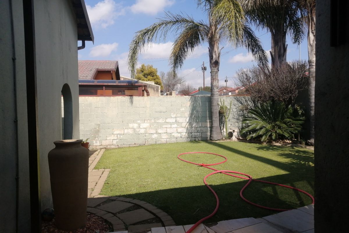 A private rear garden featuring a paved patio area, artificial lawn, and a perimeter boundary wall.