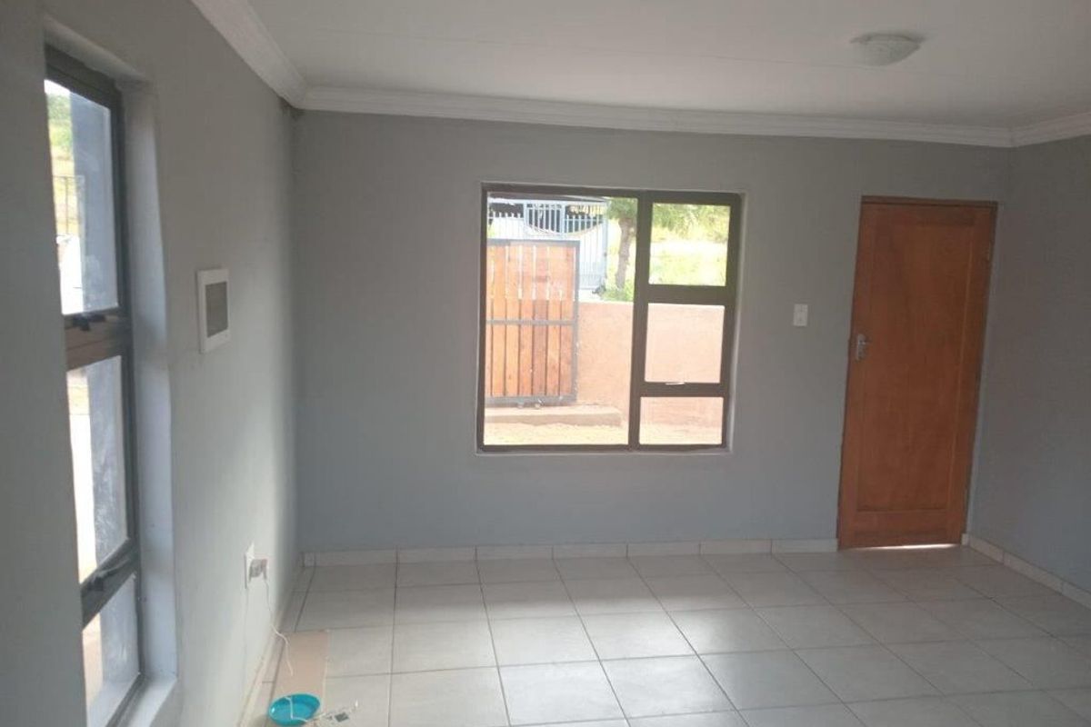 A bright, empty living area featuring neutral grey walls, tiled flooring, and aluminium-framed windows, providing a clean and versatile space.