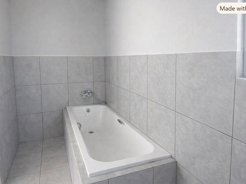 A clean, modern bathroom featuring a built-in bathtub with chrome fixtures and neutral grey ceramic tiling throughout.