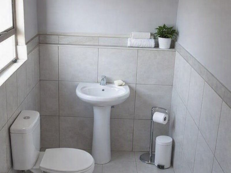A clean and functional bathroom featuring a pedestal basin, toilet, and neutral wall and floor tiling.