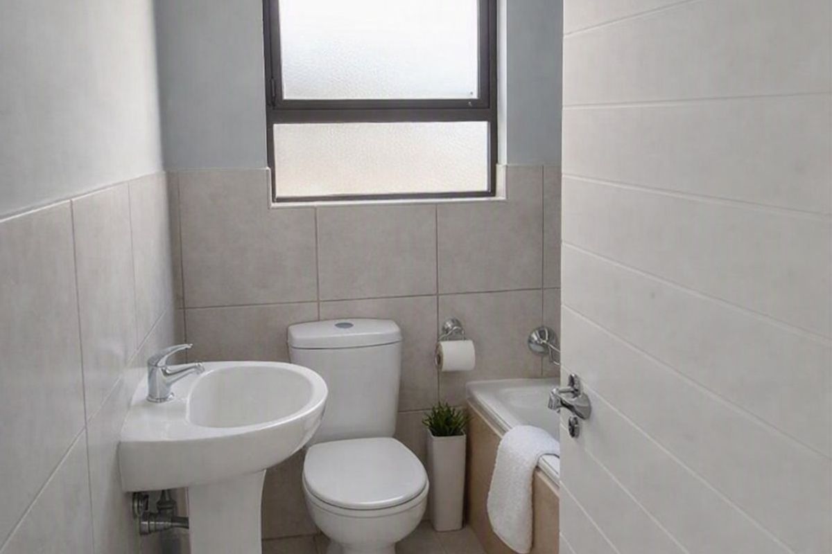 A compact, functional bathroom featuring a pedestal basin, toilet, and bathtub with neutral wall and floor tiling.