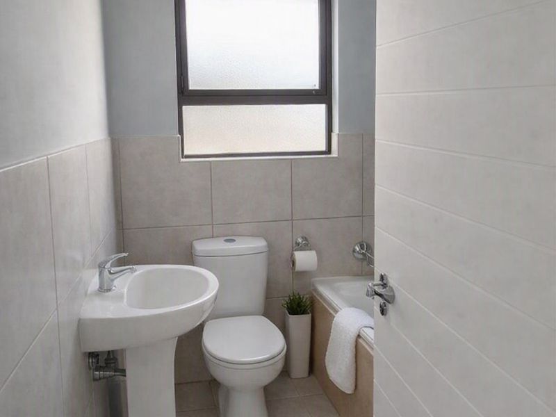 A compact, functional bathroom featuring a pedestal basin, toilet, and bathtub with neutral wall and floor tiling.