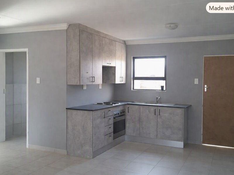 A clean, modern kitchen featuring grey cabinetry, built-in oven and hob, stainless steel sink, and neutral tiled flooring.
