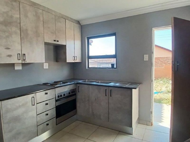 A functional kitchen featuring modern grey cabinetry, a built-in oven and hob, double sink, and tiled flooring with direct access to the exterior.